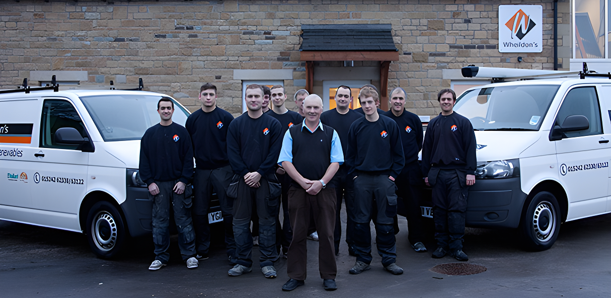 Team of heating and plumbing engineers in dark uniforms standing in front of two white branded vans