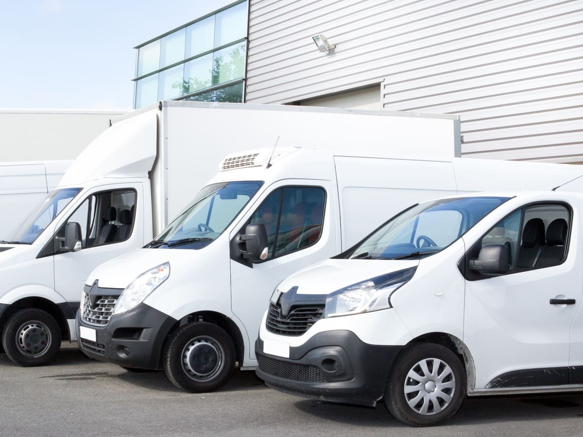 Row of white commercial delivery vans parked outside industrial warehouse building
