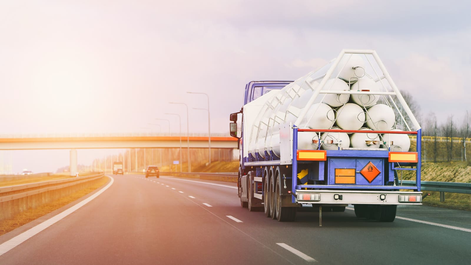 Large tanker truck carrying industrial pipes on highway during sunrise