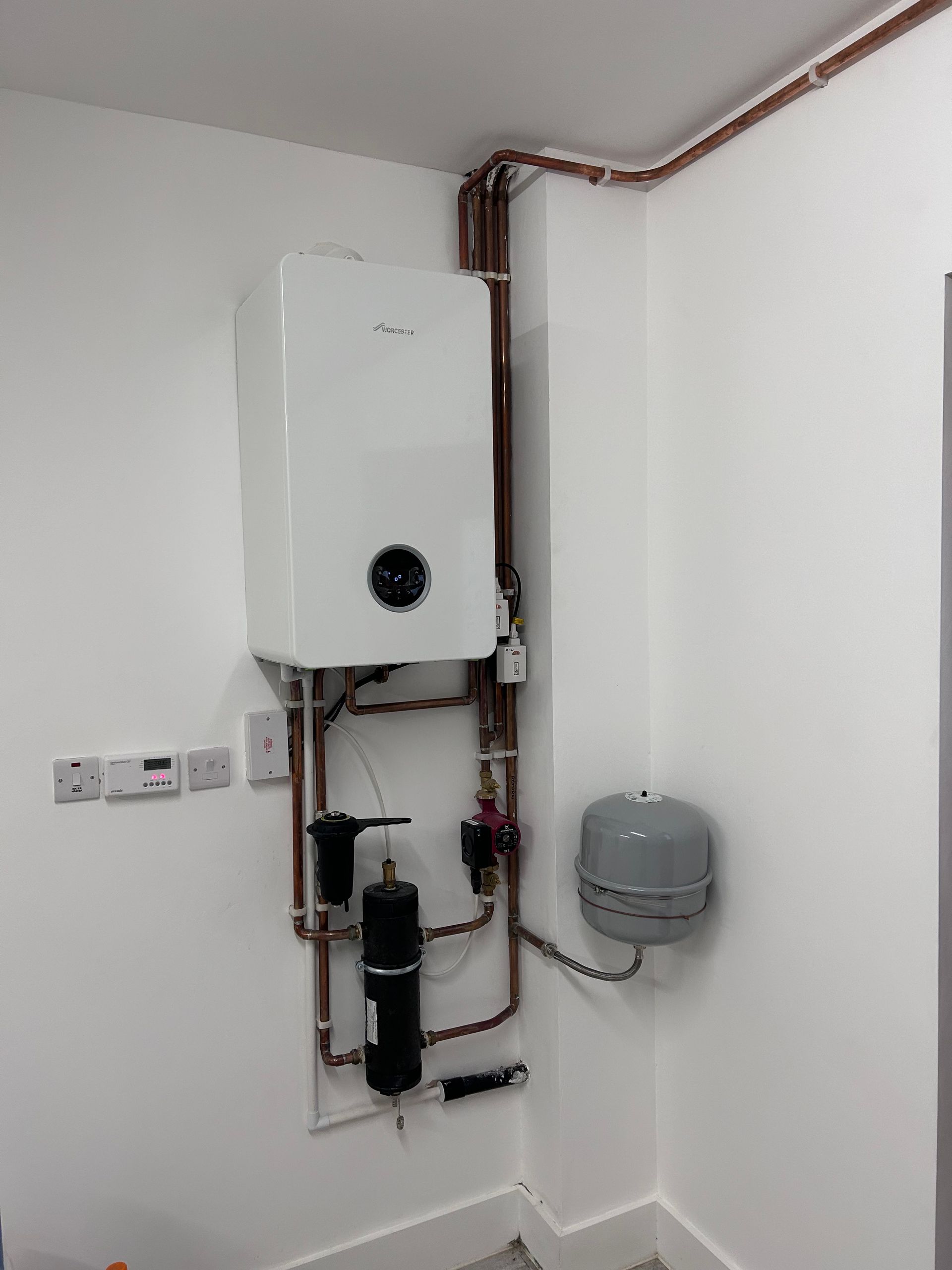 White tankless water heater mounted on wall with copper piping and gray expansion tank