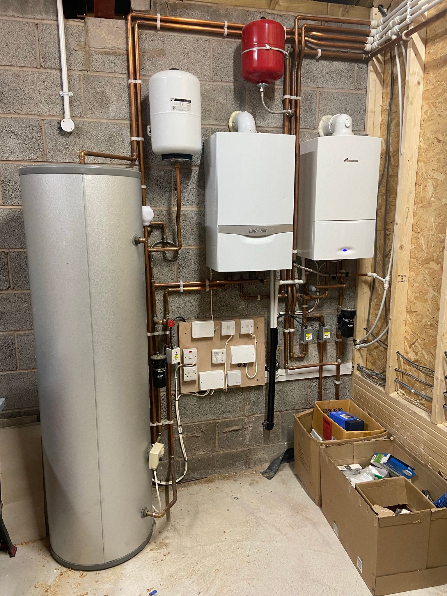 Installed heating system with two wall-mounted boilers, expansion tank, water heater, and copper piping