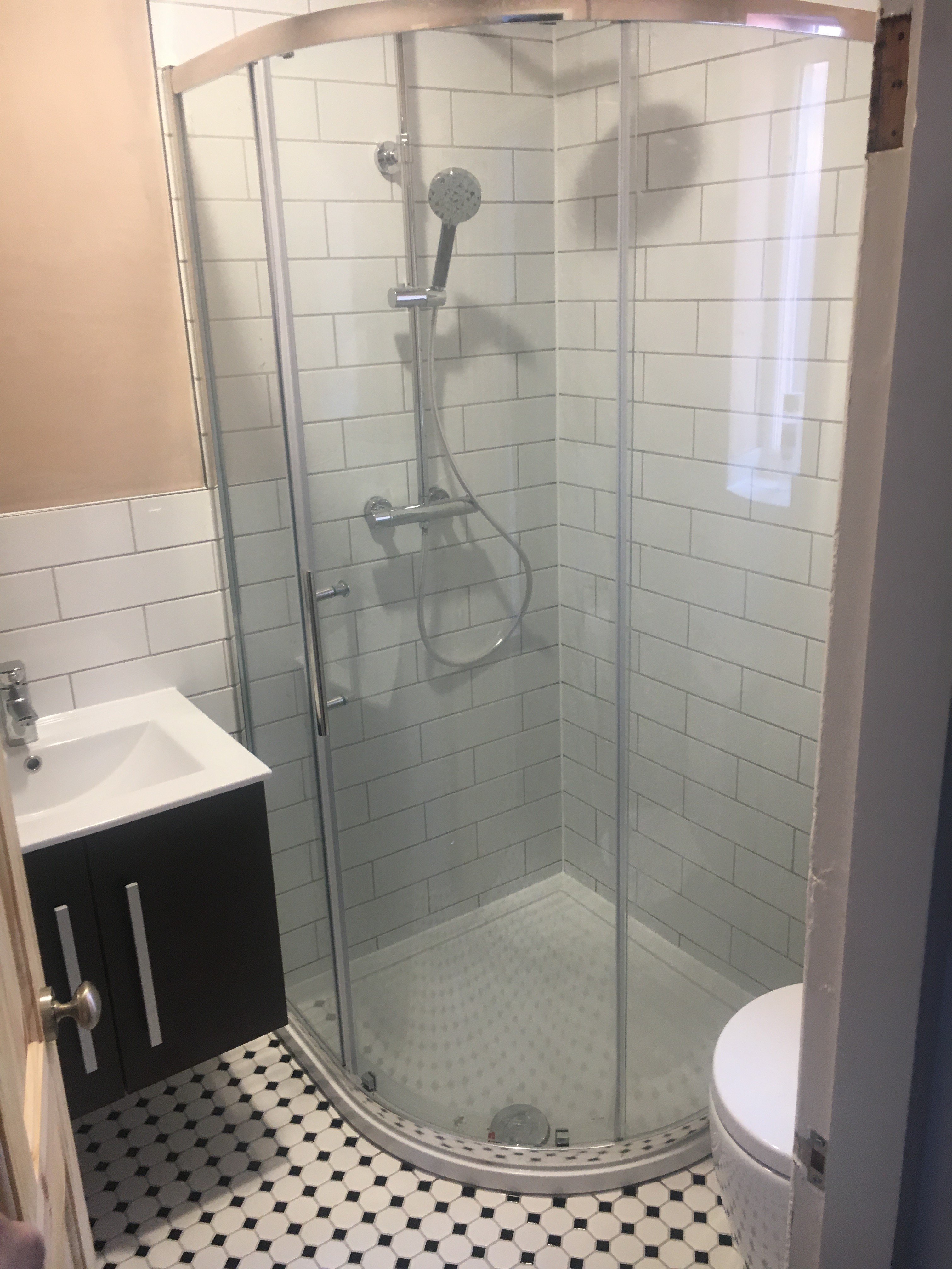 Modern bathroom with curved glass shower enclosure, white subway tile walls, dark vanity, and black and white floor tiles