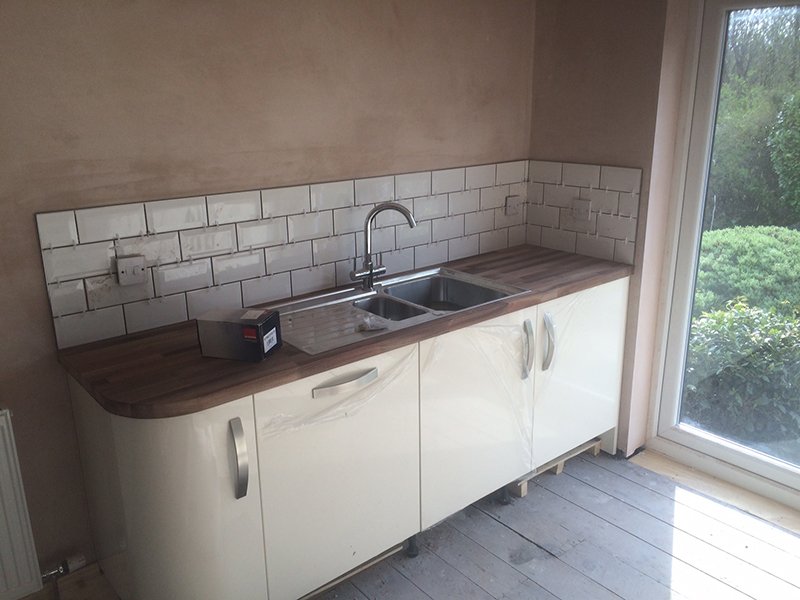 Kitchen counter with white cabinets, dark wood countertop, sink, and subway tile backsplash