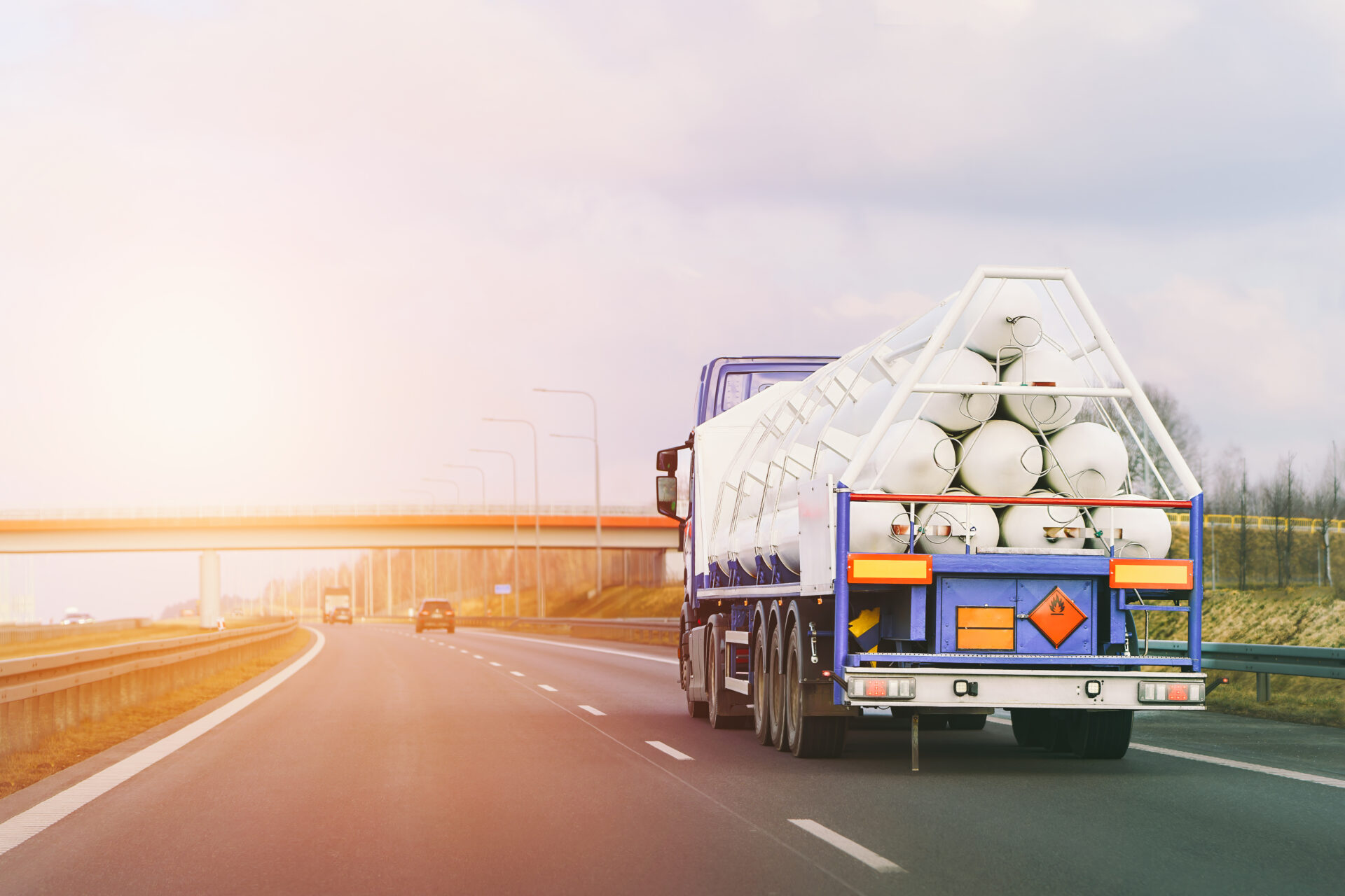 Truck transporting large rolls of white material on highway at sunset