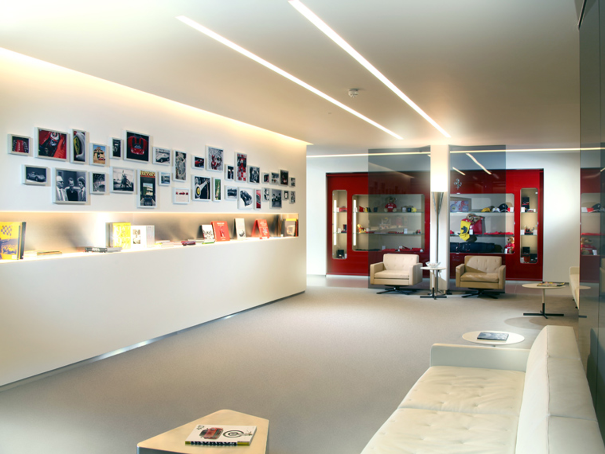 Modern showroom interior with white walls, linear ceiling lights, photo gallery wall, display shelves, red cabinetry, and seating area