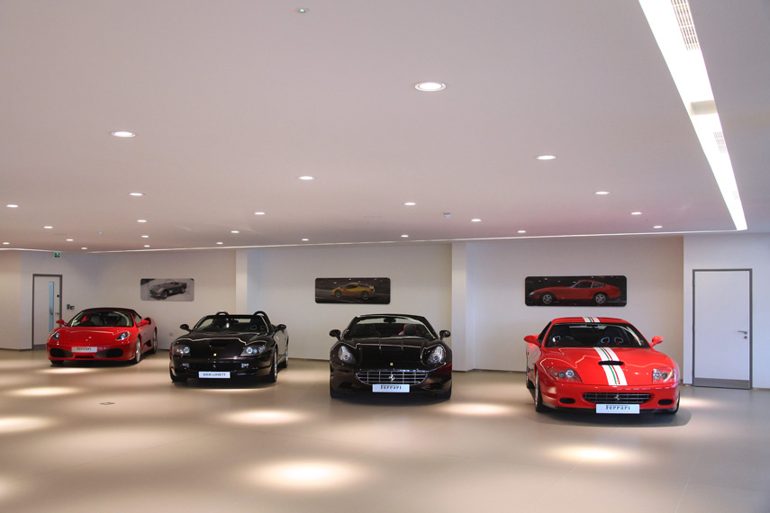Luxury sports car showroom with four cars parked under bright recessed ceiling lights