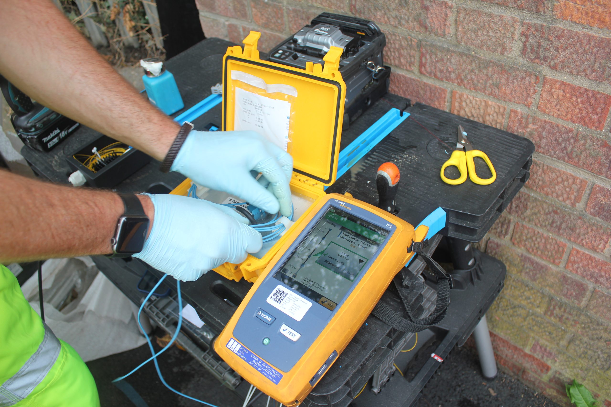 Technician in blue gloves operating yellow and orange diagnostic testing equipment on brick background
